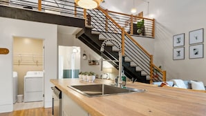 A modern kitchen with a wooden countertop, stainless steel sink, and a staircase leading to an upper level. - Alchemist @ The Vestry on Read (Columbia)