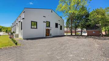 A white building with a front door and windows, surrounded by a gravel driveway and trees.