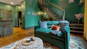 A modern living room with a teal sofa, a wooden staircase, and a bar area. - Carraway @ The Vestry on Read (Columbia)