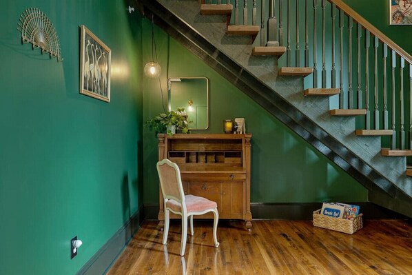 Una habitación con un escritorio de madera, una silla, un espejo y una escalera con paredes verdes y escalones de madera.