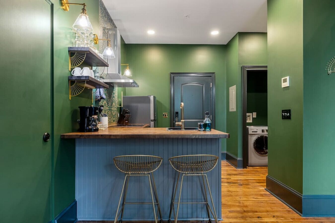 Une cuisine avec un coin bar, deux tabourets, un lave-linge et une porte.
