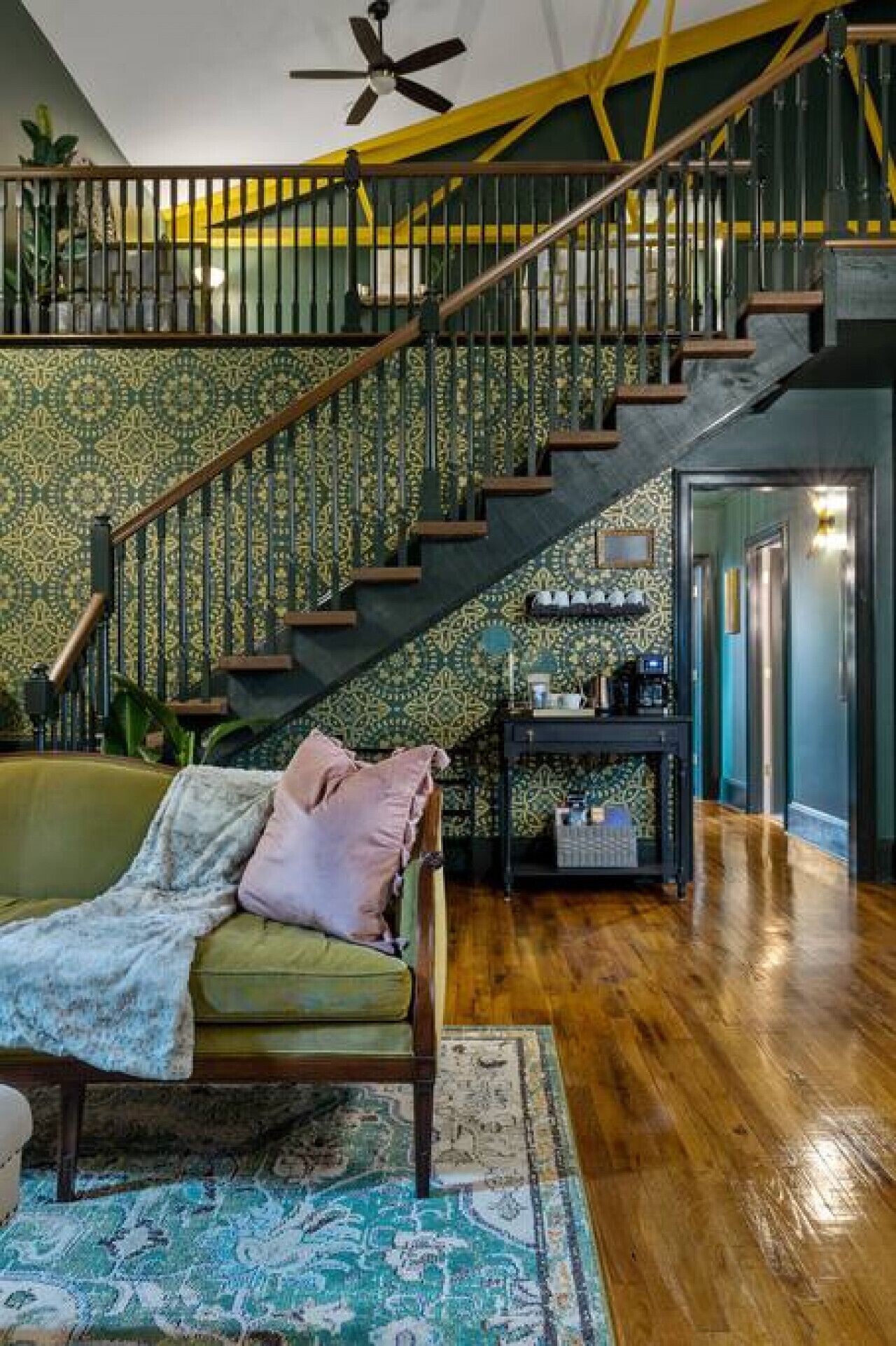 Un vaste espace de vie avec un escalier menant à un niveau supérieur, un canapé vert et un tapis à motifs.