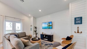 Una sala de estar con un sofá, dos sillones de mimbre, un mueble de entretenimiento negro y un televisor en la pared.