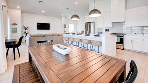 Una cocina moderna con armarios blancos, una mesa de comedor de madera e iluminación colgante.