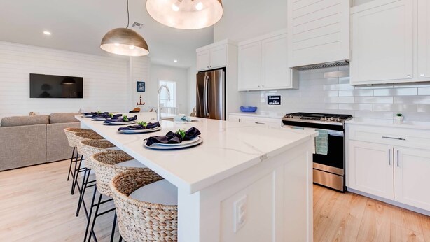 Una cocina moderna con armarios blancos, una isla central con taburetes de bar, electrodomésticos de acero inoxidable e iluminación colgante.