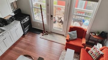 Et moderne køkken med komfur og skabe, et spiseområde med bord og stole, samt en rød sofa med et mønstret pude.
