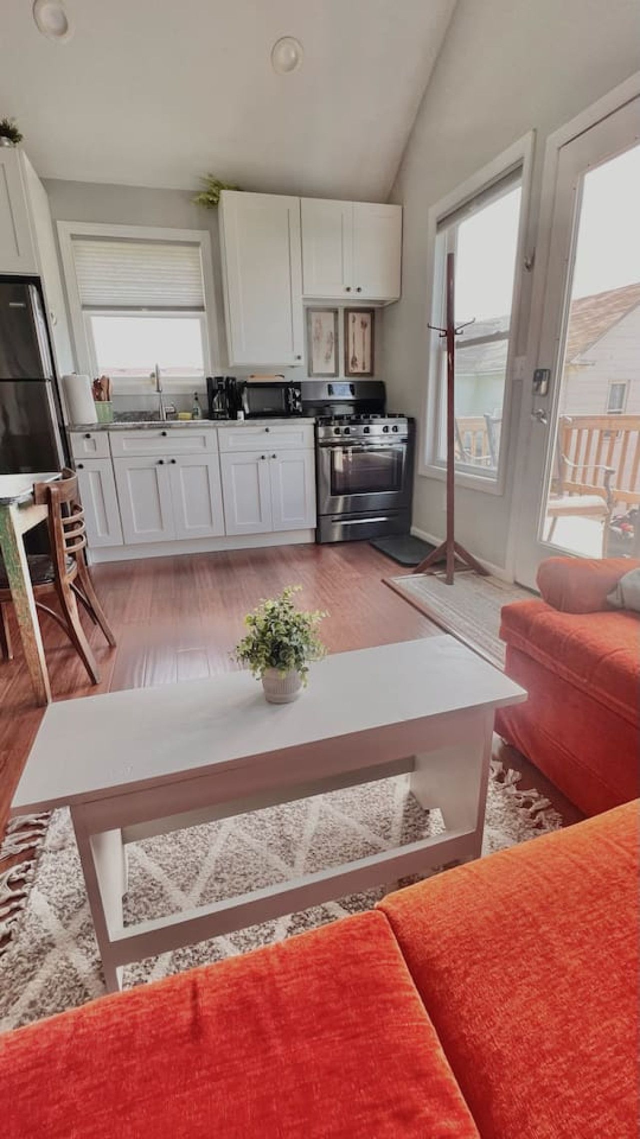 Cocina moderna con armarios blancos, estufa de acero inoxidable y comedor con sofá rojo y mesa de centro blanca.