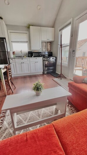 A modern kitchen with white cabinets, a stainless steel stove, and a dining area with a red sofa and a white coffee table.
