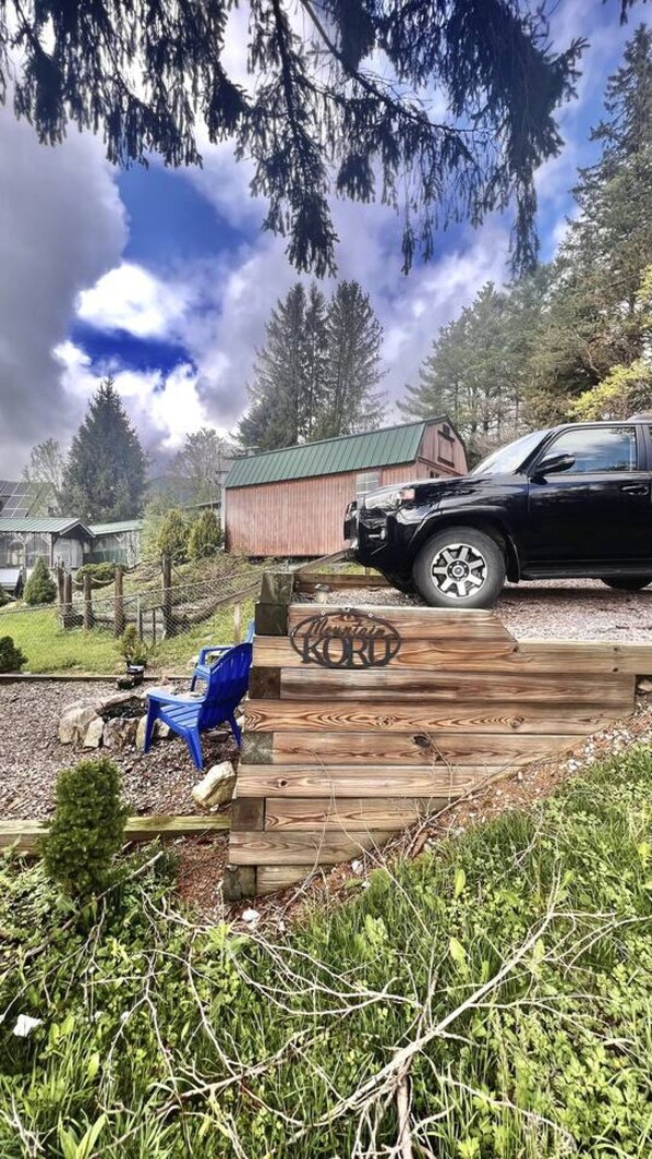 A wooden deck with a logo, a black vehicle, and a green-roofed building in a wooded area.