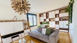A modern living room with a grey sofa, a glass coffee table, and a wooden floor. There is a large wooden shelf unit with various decorative items and a hanging light fixture. - Maison au Calme et en Ville (Annecy)