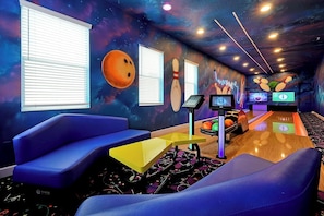 A bowling alley with blue seating, bowling lanes, and a cosmic-themed wall mural.