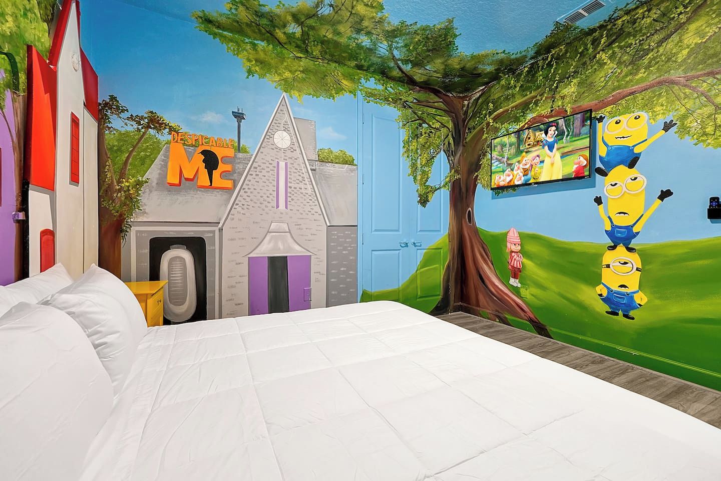 A bedroom with a bed, a mural of a tree, and Minion characters.