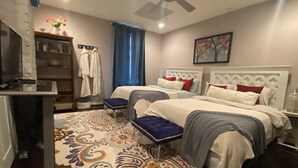 Una habitación de hotel con dos camas, ventilador de techo, estantería y alfombra estampada.