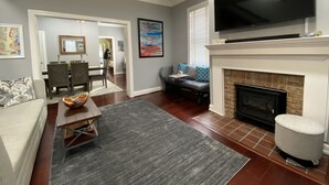 Una sala de estar con chimenea, un televisor montado encima, un sofá, una mesa de centro y una zona de comedor al fondo.