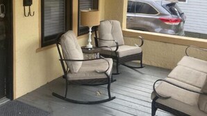 Une véranda avec deux fauteuils à bascule et une table, une lampe et une boîte aux lettres fixée au mur.