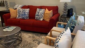 Un salon avec un canapé rouge, deux fauteuils, une table basse et un tableau accroché au mur.