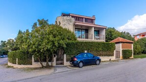 A two-story house with a stone facade, a balcony, and a car parked in front.