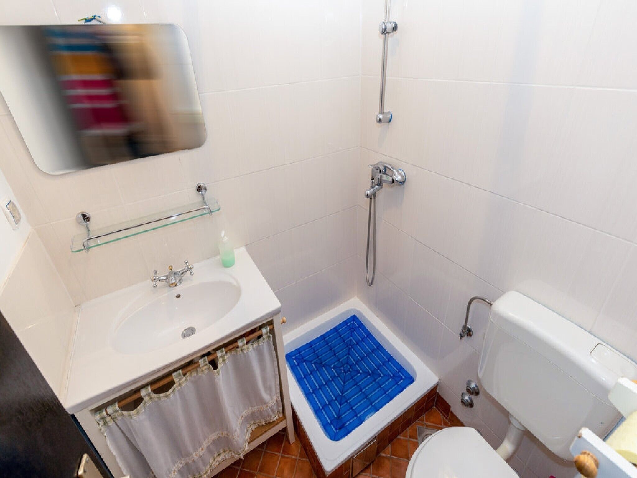 Et badeværelse med hvid vask, glas hylde, brusebad og toilet.