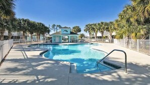 A swimming pool with a small building in the background, surrounded by palm trees and a white fence. - SEASHORE · *Summer’s Special | King Bed| Cvrd Back Porch* (Panama City Beach)