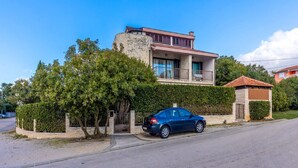 A two-story house with a balcony, a car parked in front, and a hedge. - Apartments Ilija Njavro - Studio Apartment (Jadranovo)
