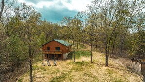 A wooden cabin with a porch and two chairs, surrounded by trees and a grassy area. - Secluded Getaway with Private Meramec River Access and Floating (Steelville)