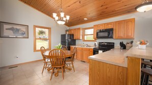 A kitchen with wooden cabinets, a dining table with chairs, a chandelier, and a large window. - Secluded Getaway with Private Meramec River Access and Floating (Steelville)