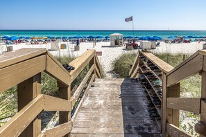 A wooden boardwalk leading to a beach with umbrellas and a lifeguard station. - At Last Romantic Luxury Beach Front, Fireplace Free BeachChairs & Umbrella (Panama City Beach)