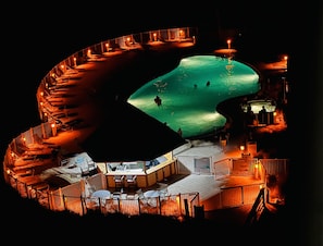 Uma piscina com formato singular, rodeada por espreguiçadeiras e mesas, com uma placa que indica 'NO DIVING'.