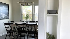 Un coin repas avec une table ronde et des chaises, un luminaire suspendu et une fenêtre donnant sur la forêt.