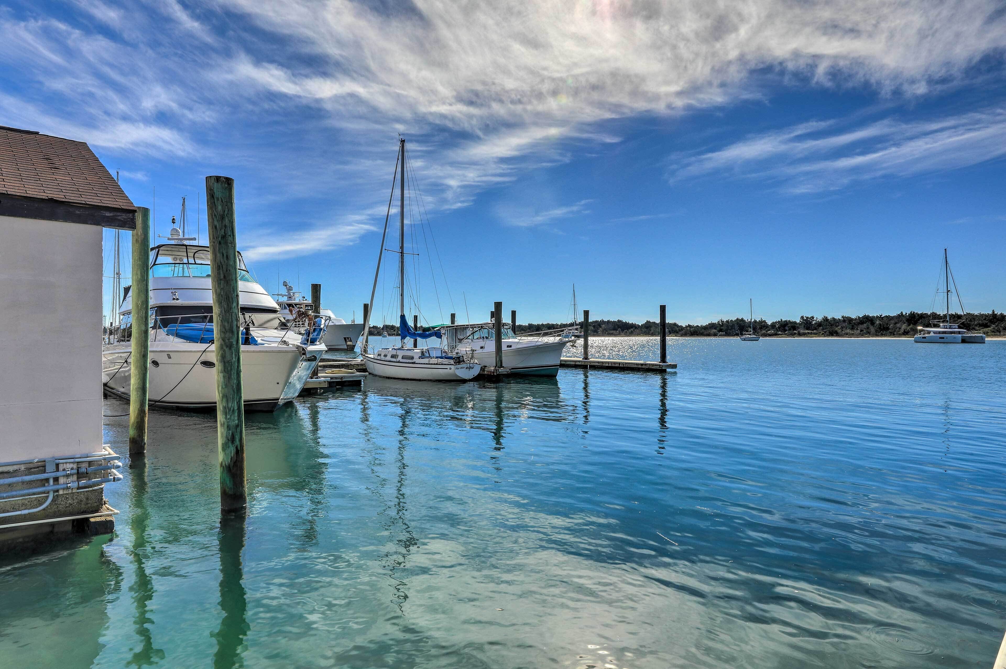 A marina with several boats docked, clear blue water, and a building on the left.