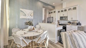 A modern kitchen with white cabinetry, a central island, and a dining area with wicker chairs. - The Beaufort Flat Near Downtown & Waterfront! (Beaufort)