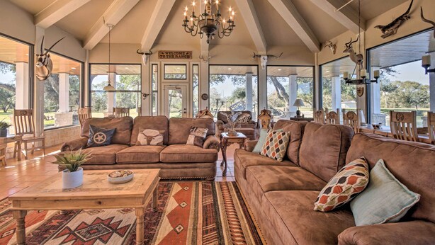 A spacious living room with a large brown sectional sofa, a wooden coffee table, and a patterned rug. There are multiple windows providing natural light and views of the outdoors. - Lakefront Wallis Ranch w/ Private Beach & Patio! (Wallis)