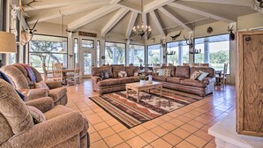 A spacious living room with a high ceiling, large windows, and a fireplace. There are multiple seating areas, including sofas and chairs, and a coffee table. - Lakefront Wallis Ranch w/ Private Beach & Patio! (Wallis)