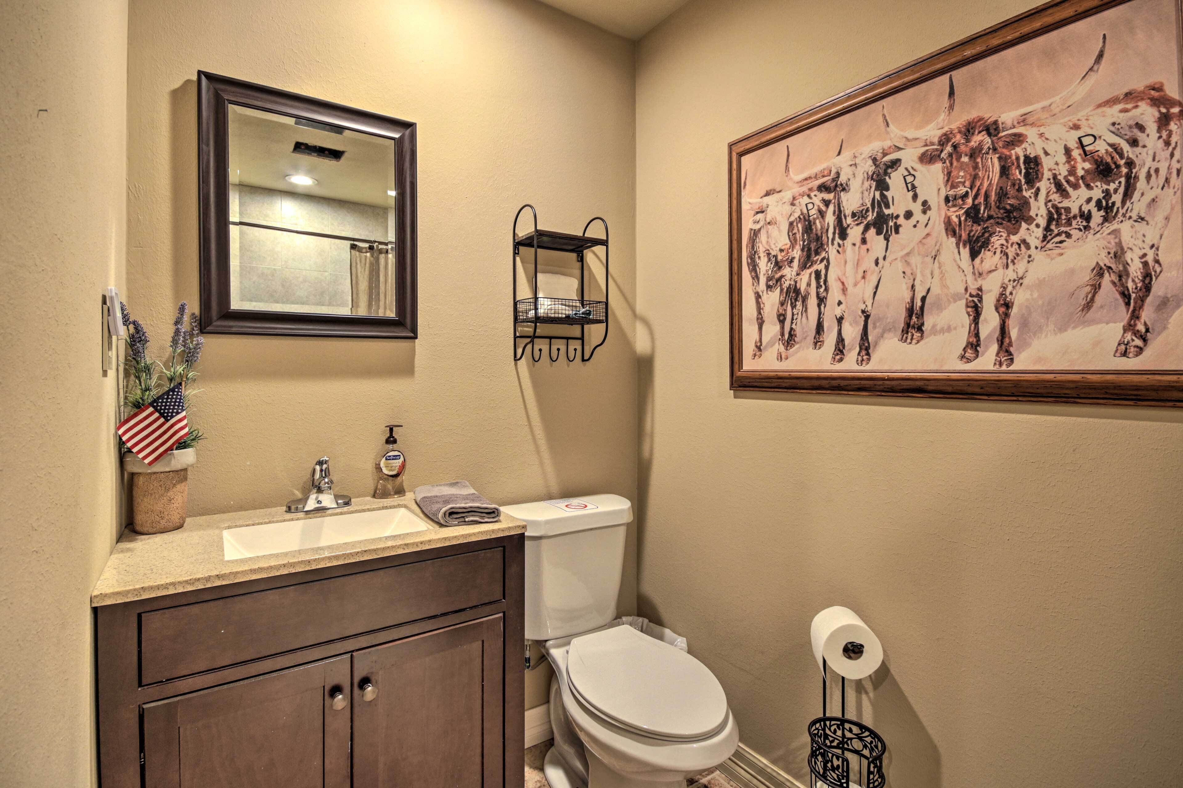 A bathroom with a sink, mirror, toilet, and a framed painting of cattle.