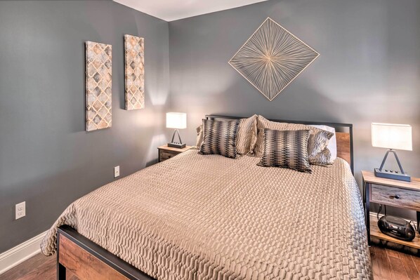 A bedroom with a large bed, two bedside tables, a wall-mounted lamp, and two wall art pieces. - Bristol Escape w/ Patio, 2 Mi to Downtown! (Bristol)