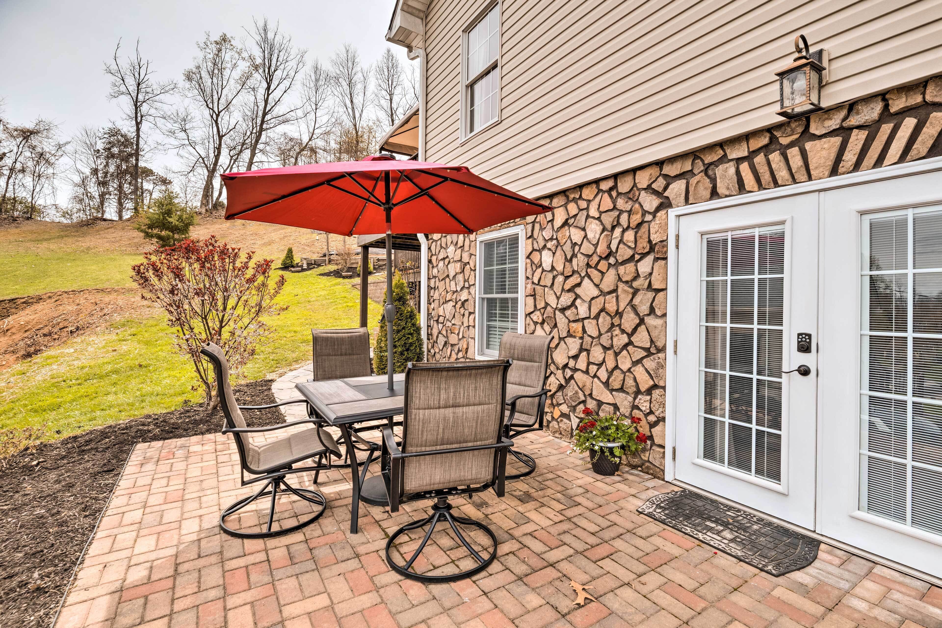 An outdoor patio with a table and chairs, a red umbrella, and a stone wall.