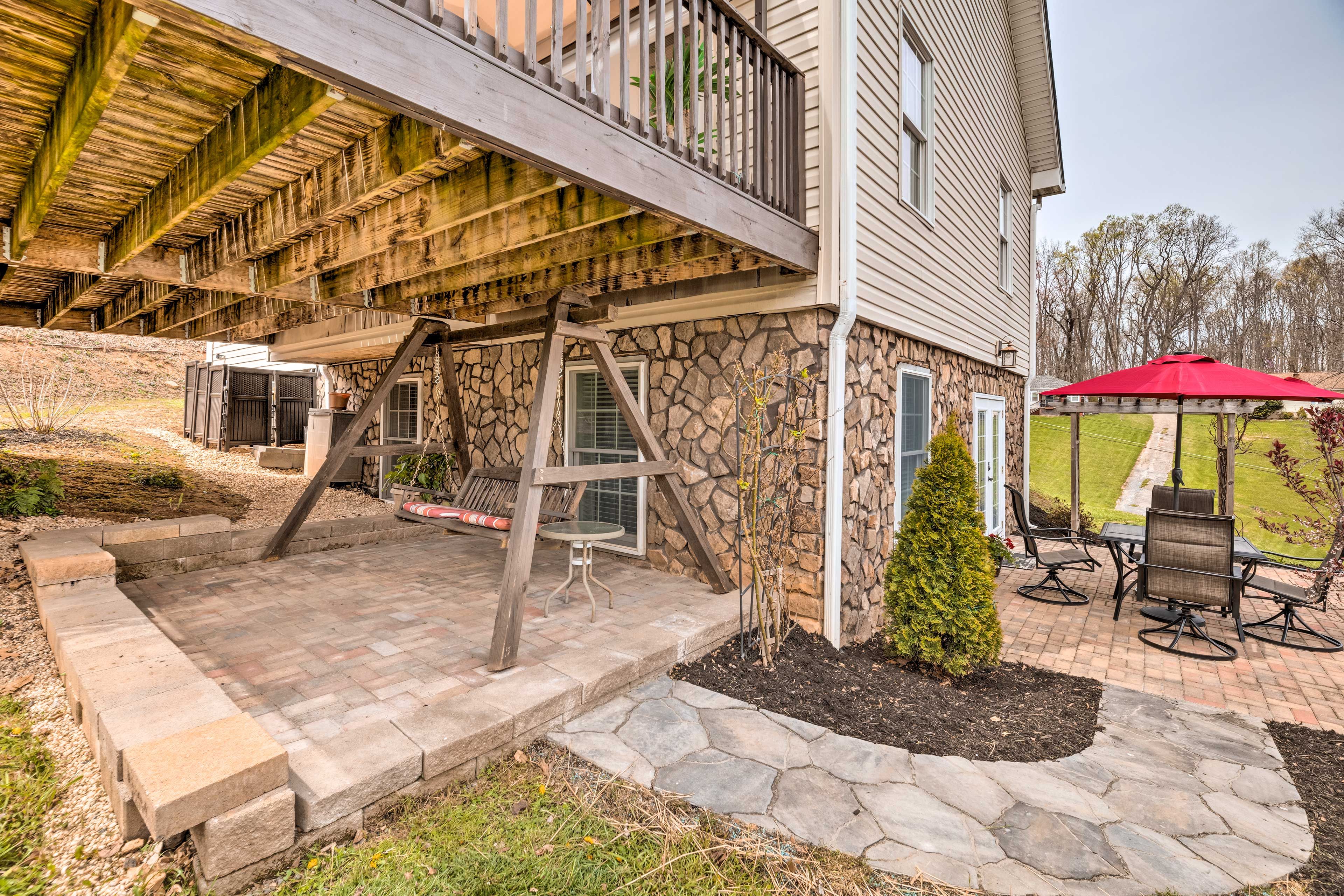 A covered outdoor patio with stone steps, a wooden swing set, and a red umbrella.
