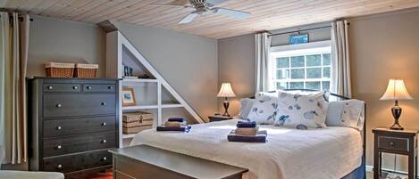 Ein Schlafzimmer mit einem Bett, Nachttischen, einer Kommode, einem Deckenventilator und einem Fenster mit Vorhängen.
