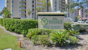 Schild für das Hotel The Indies The Dunes, mit einer Palme und Grünpflanzen im Vordergrund.
