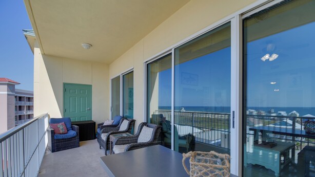 Ein Balkon mit Korbmöbeln, einer grünen Tür und Blick aufs Meer.