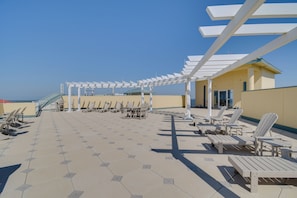 A sunlit outdoor seating area with hexagonal tiles, white pergolas, and lounge chairs. - Beachfront Gulf Shores Family Escape: Pool Access (Gulf Shores)