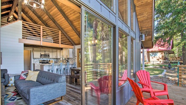 Una cabaña moderna con cocina, sala de estar con sofá y sillones, y una terraza con sillas rojas.