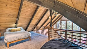 Un dormitorio acogedor en el desván, con techo de madera, una cama, una mesita y vistas al exterior a través de amplias ventanas.