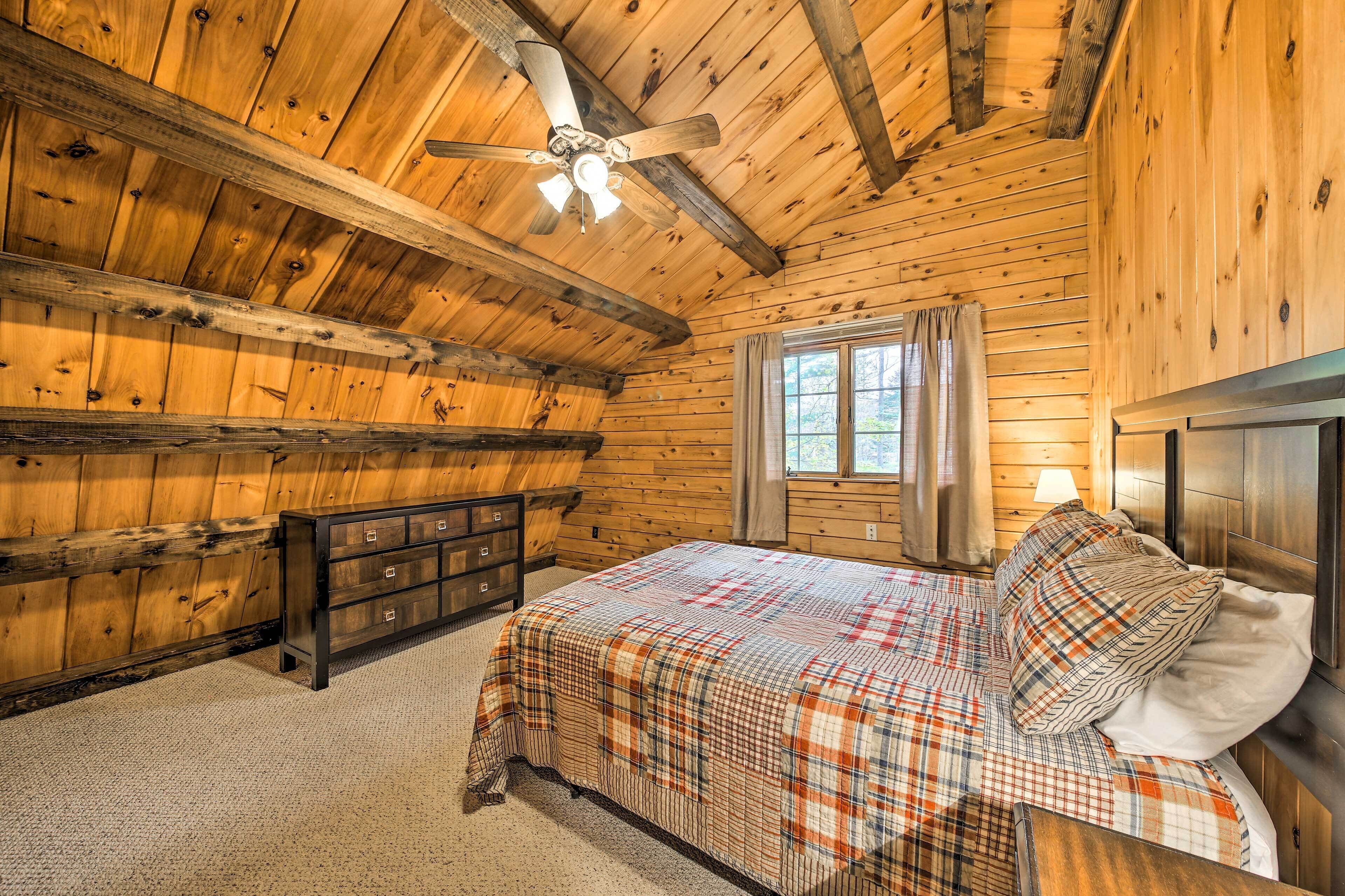 Een slaapkamer in een houten blokhut, met een bed, een dressoir en een plafondventilator.