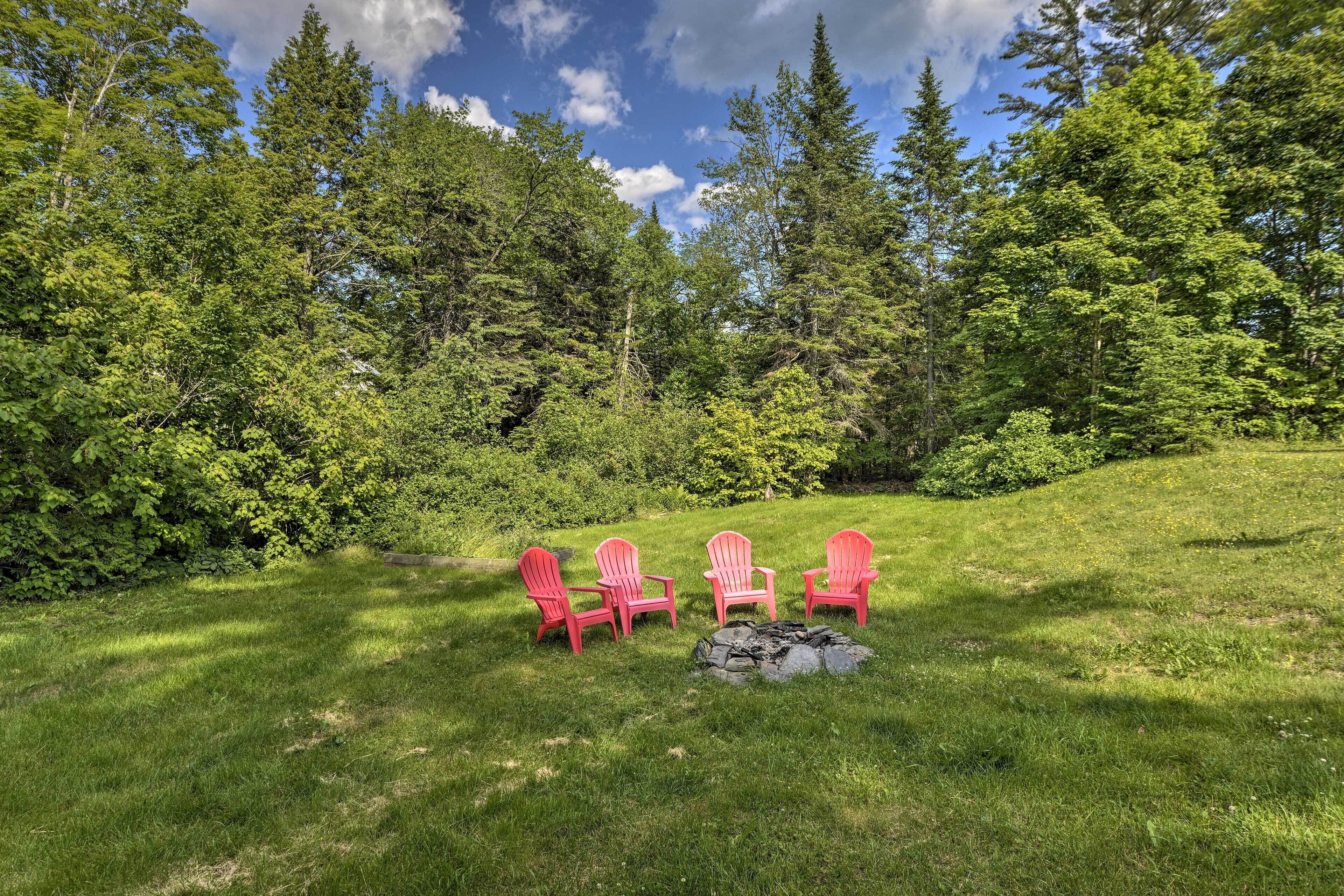 A grassy area with four red Adirondack chairs arranged in a semi-circle around a stone fire pit.