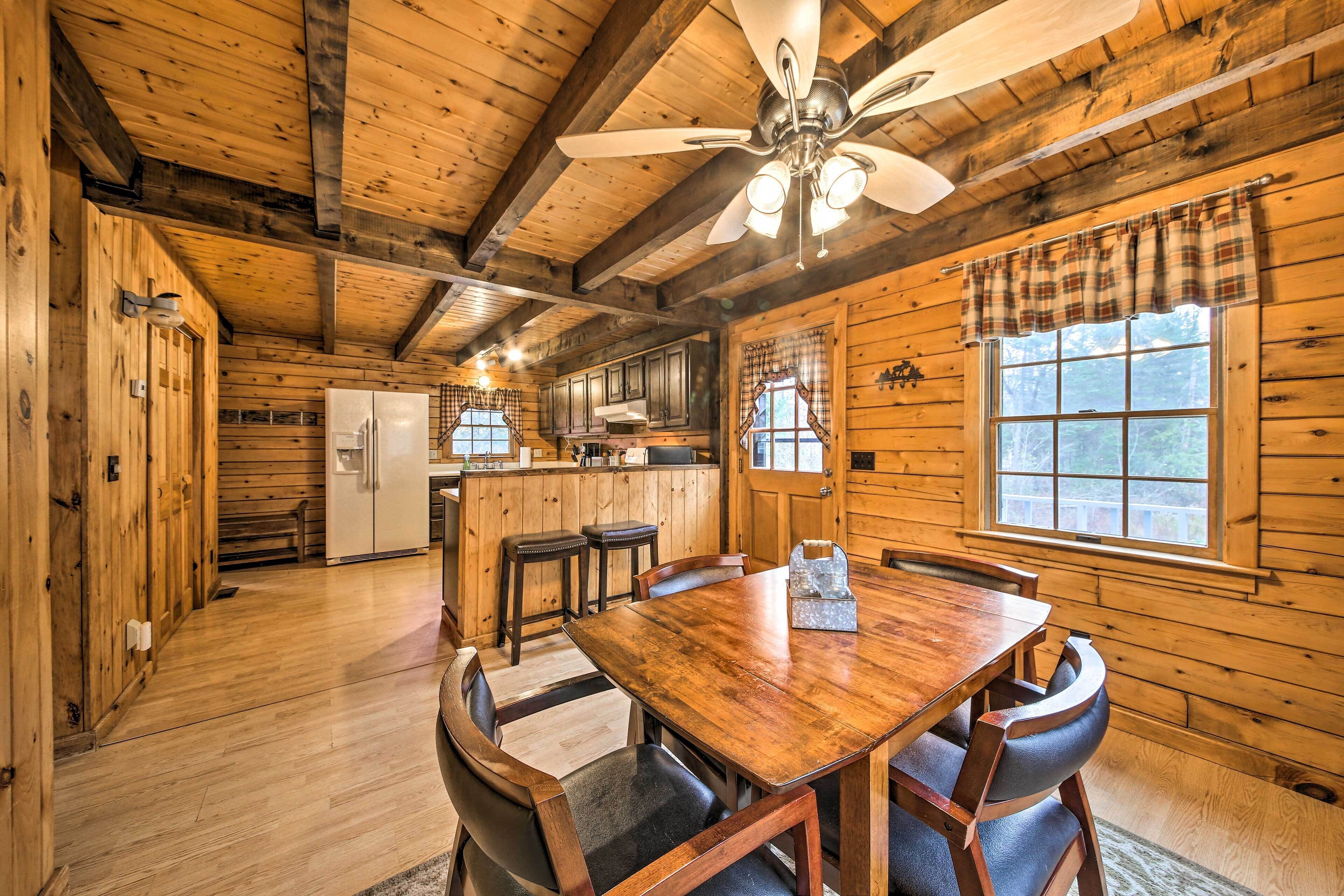 Interior de una cabaña de madera con comedor, cocina y un ventanal grande.