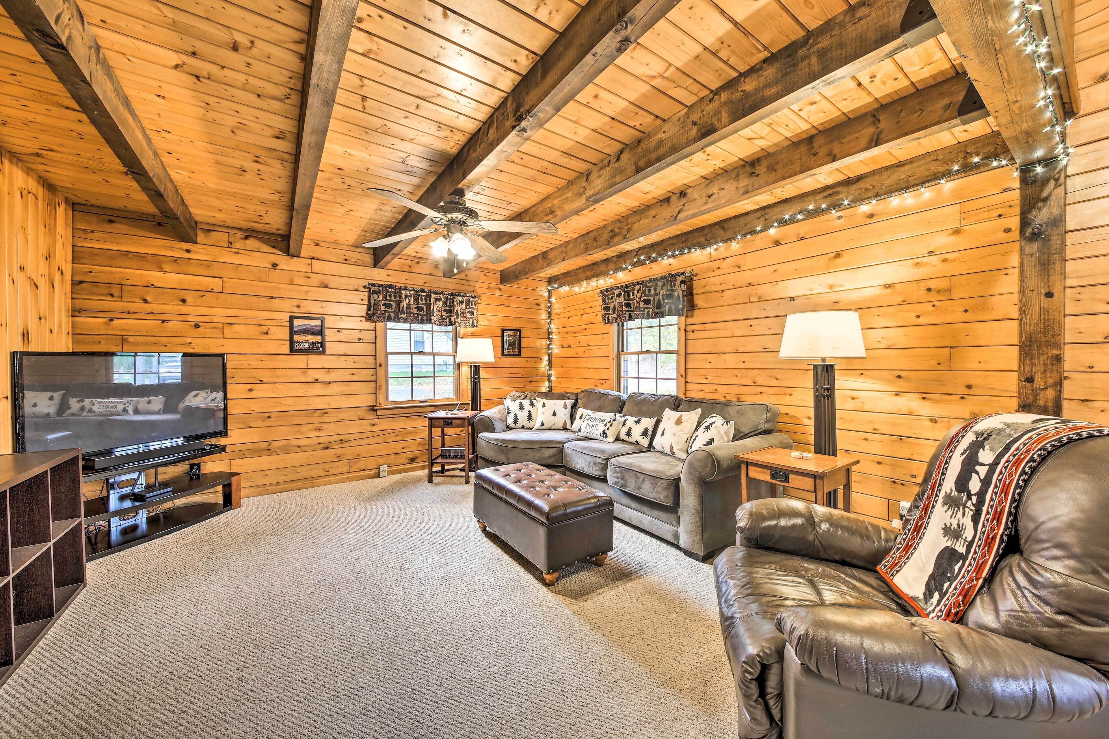 A log cabin interior with a television, leather sofas, and a ceiling fan.