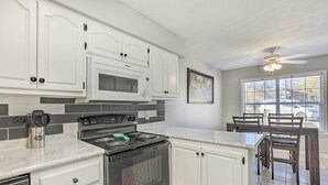 Una cocina con armarios blancos, un microondas, una estufa y un comedor con mesa y sillas.