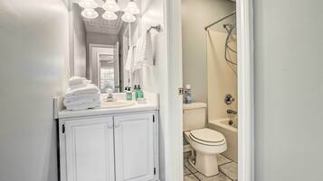A bathroom with a white vanity, a mirror, a sink, and a toilet. There are towels stacked on the vanity and a shower curtain visible in the background.