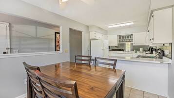 A modern kitchen with white cabinets, a wooden dining table, and a built-in oven.